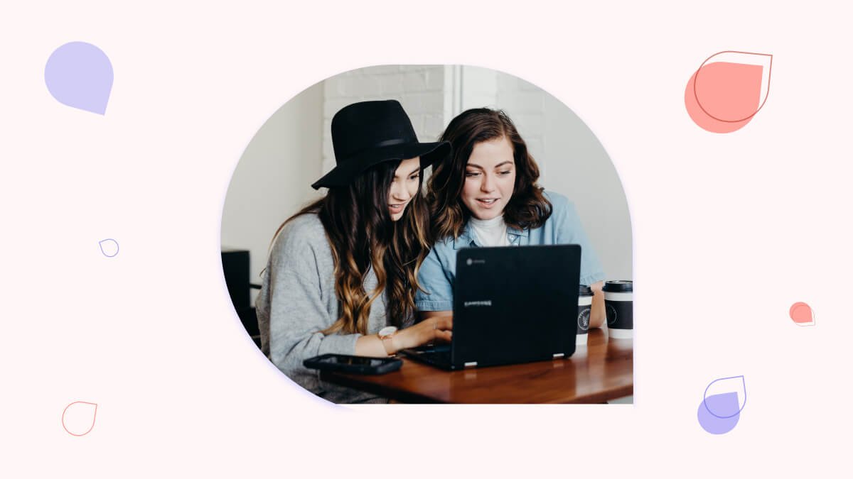 two women sitting at a table looking at a laptop