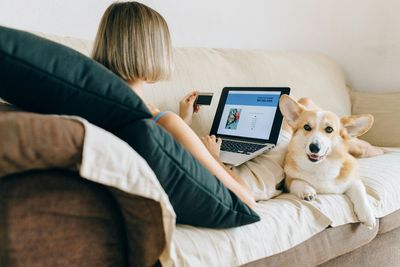 a woman sitting on a couch with a laptop and a dog