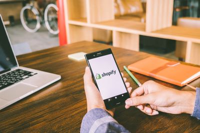 a person sitting at a table with a cell phone on Shopify