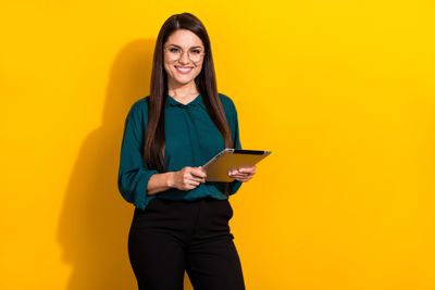 a woman standing in front of a yellow wall holding a tablet