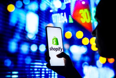 a person holding up a cell phone with the word shopify on it
