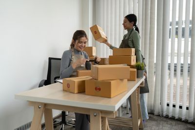 two women work on an eCommerce order, with multiple boxes on a table and a laptop