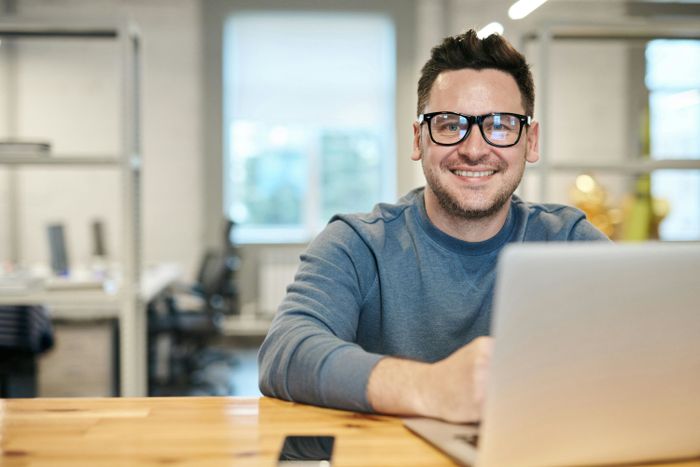 A man is smiling while sitting at a table with a laptop preview image
