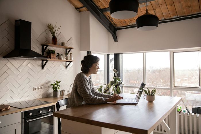 a woman sitting at a kitchen counter using a laptop preview image