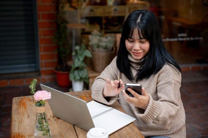 A social media freelancer works on her laptop and phone at a coffee shop preview image