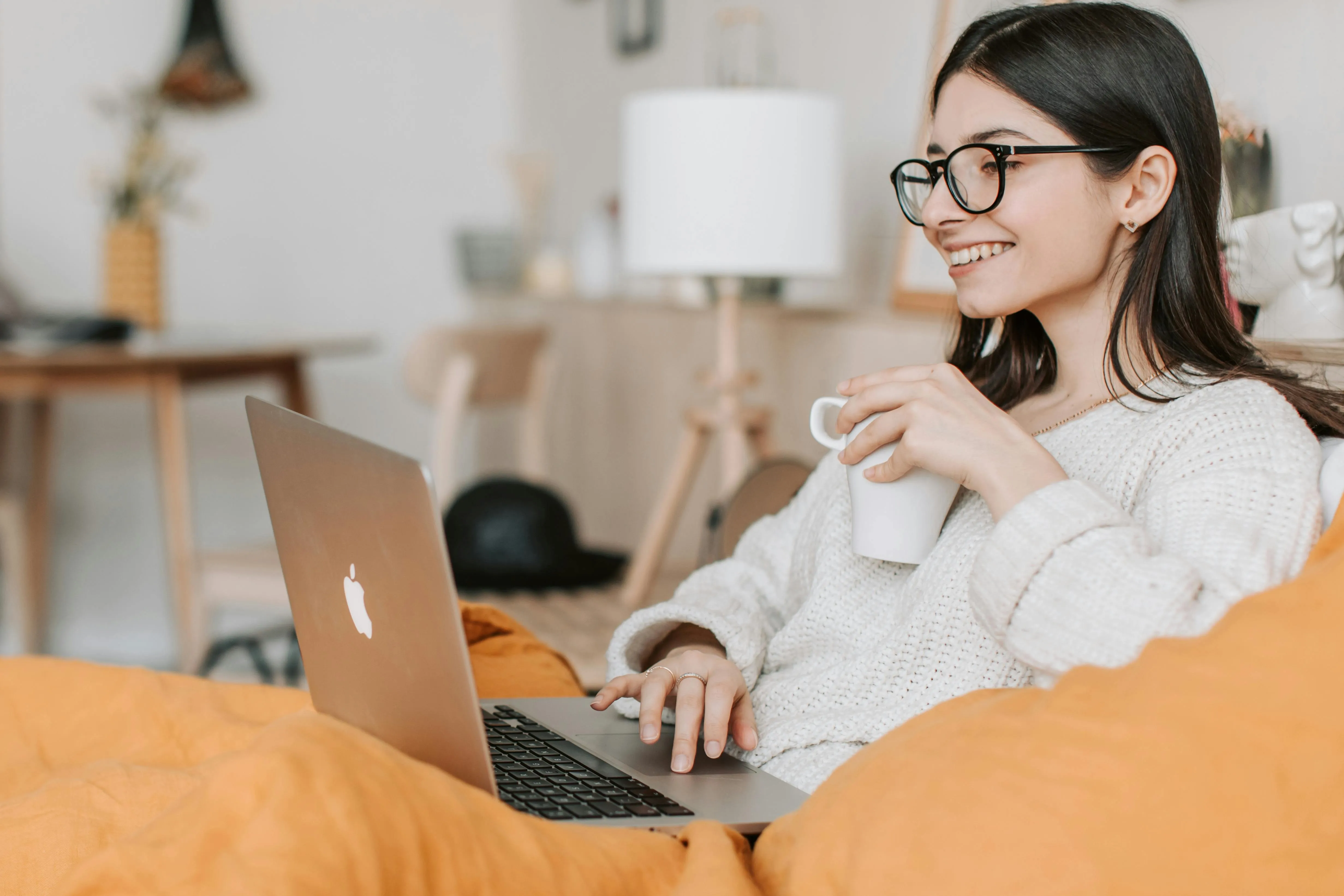 A woman sitting on a couch working on a laptop while holding a coffee cup